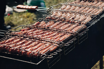 Close-up of delicious chicken or pork sausages on BBQ. Unrecognizable cook preparing tasty sausages on grill.