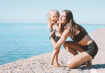 Young fit woman mom with little cute girl exercising on sea beach together, healthy lifestyle