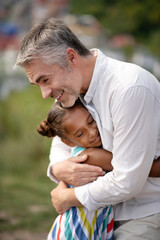 Beaming loving father hugging his cute dark-skinned daughter