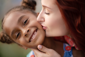 Adopted girl smiling broadly while mother kissing her