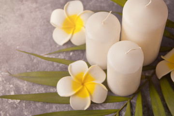 Three white candles, plumeria flower and palm leaf on the gray background. Spa therapy concept. Top view.