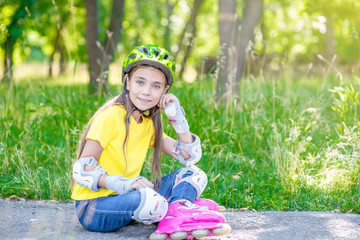 Smiling girl in a protective helmet and protective pads for roller skating sitting on the road. Empty space for text