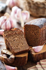 Loaf of rye bread with cloves of garlic on a rustic wooden cutting board