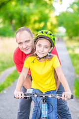 Happy family. Smiling man teaches his daughter to ride a bicycle in the summer park