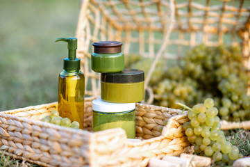 Jars and bottles with cosmetics or various health products made on the basis of grapes on the wicker baskets with wine grapes outdoors