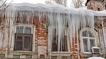 Huge sharp icicles hang dangerously from the roof of an old house.