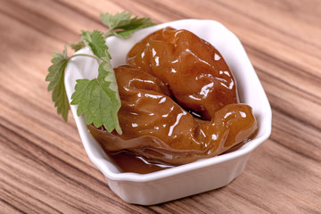 Pear jam with fresh mint leaves in a white faience bowl on a wooden surface