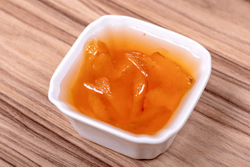 Sweet peach jam in a porcelain white bowl on a wooden surface