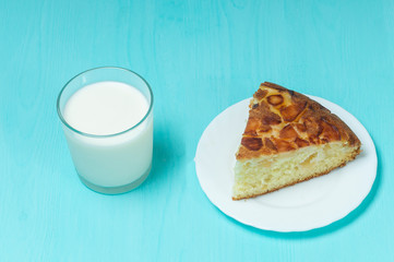 Apple pie on a white plate a glass of milk, on a blue wooden background close-up