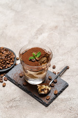 Portion of Classic tiramisu dessert in a glass cup on stone serving board on concrete background