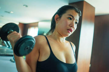 Fototapeta na wymiar mirror portrait of young pretty and fit Asian Korean woman working hard at hotel gym or fitness center lifting dumbbell doing body building indoors workout