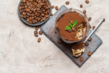 Portion of Classic tiramisu dessert in a glass cup on stone serving board on concrete background