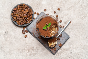 Portion of Classic tiramisu dessert in a glass cup on stone serving board on concrete background