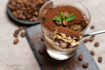Portion of Classic tiramisu dessert in a glass cup on stone serving board on concrete background
