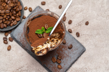 Portion of Classic tiramisu dessert in a glass cup on stone serving board on concrete background