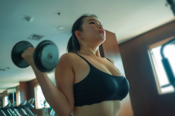 Fototapeta na wymiar mirror portrait of young pretty and fit Asian Chinese woman working hard at hotel gym or fitness center lifting dumbbell doing body building indoors workout