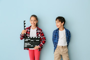 Cute little children with movie clapper on color background