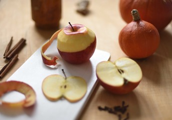 Peeled apple on cutting board surronded by pumpkins, spices and kitchen stuff