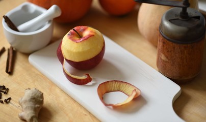 Peeled apple on cutting board surronded by pumpkins, spices and kitchen stuff