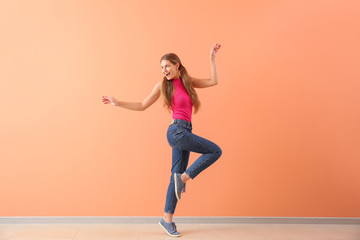 Fototapeta na wymiar Beautiful young woman dancing against color wall
