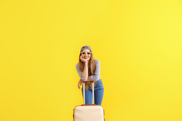Happy young woman with suitcase on color background