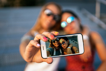 Cheerful women sitting on bridge and using cellphone