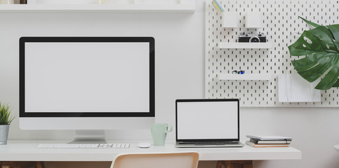 Desktop computer and blank screen laptop with copy space and office supplies in minimal office room