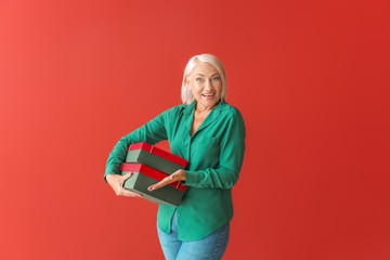 Stylish mature woman with gift boxes on color background