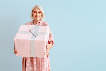 Mature woman with gift box on color background