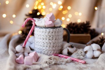 Holiday christmas composition with mug in knitted white sweater with strong hot coffee and marshmallows. Rustic decor, cotton, cones, cinnamon, anise. Lights on. Cozy quite romantic atmosphere