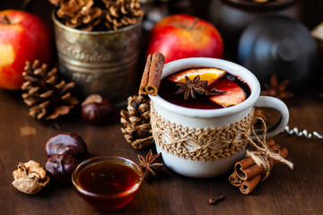 Cozy time at home with a metal mug of hot mulled wine. Autumn, warm clothes, natural ingredients, spice, fruit and honey. Corkscrew to open wine. Rustic decor, festive mood