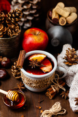 Cozy time at home with a metal mug of hot mulled wine. Autumn, warm clothes, natural ingredients, spice, fruit and honey. Corkscrew to open wine. Rustic decor, festive mood