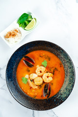 Vietnamese Tom Yum soup with seafood. Red soup with shrimp, scallop, mussels, salmon in a dark stylish bowl on a marble table. Minimalosm food photo concept. bouillabaisse