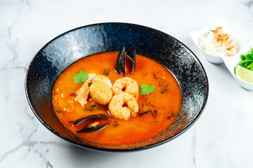 Vietnamese Tom Yum soup with seafood. Red soup with shrimp, scallop, mussels, salmon in a dark stylish bowl on a marble table. Minimalosm food photo concept. bouillabaisse