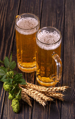 Two glass mugs with transparent beer and stalks of wheat and  hops stand on  wooden rustic textured table. © rozaivn58