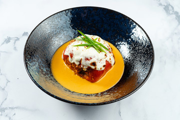 Stuffed peppers with mozzarella on top with yellow sauce in a stylish black bowl on a marble background. Russian homemade cuisine. Restaurant food style