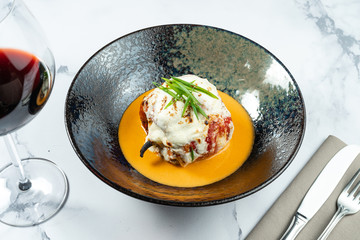 Stuffed peppers with mozzarella on top with yellow sauce in a stylish black bowl on a marble background. Russian homemade cuisine. Restaurant food style