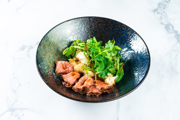 Warm salad with roast beef, crackers, arugula and sauce in a black bowl on a marble table. Tasty and healthy snack for lunch. Food photo background for menu or recipe. Restaurant