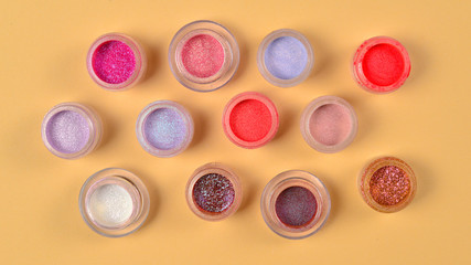 Cosmetics. Makeup. Jars with  crumbly bright shadows, glitter. Pink,peach, golden colors on beige background. Closeup. Space for text or design.
