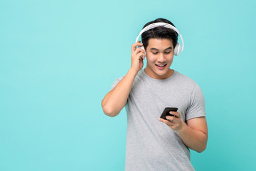 Happy young Asian man wearing wireless headphones listening to music from smartphone