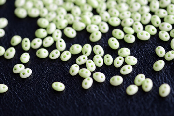 Twin beads light green color scattered on a dark surface close up