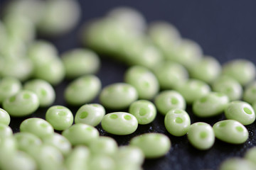Twin beads light green color scattered on a dark surface close up