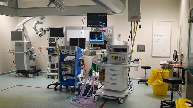 Fully equipped modern surgical operating room depicting anaesthesia machine various monitors and an operating microscope in the background