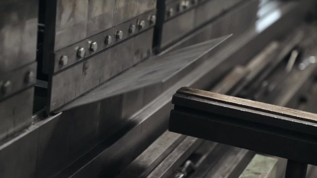 Gloved hand positioning metal in machine to be bend, industrial plant.