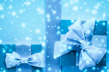Winter holiday gifts and glowing snow on frozen blue background, Christmas presents surprise