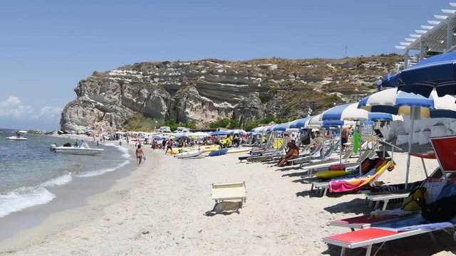 Panoramic view of the Italian coastline with tuff headland and beach with sunbeds and umbrellas - Real Time in 4k