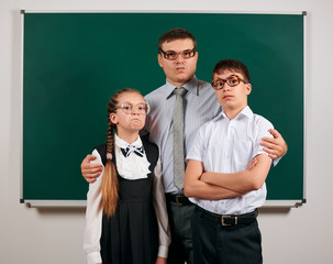 Portrait of a teacher, schoolboy and schoolgirl with old fashioned eyeglasses posing on blackboard background - back to school and education concept