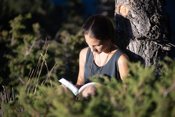 Chica adolescente leyendo un libro el exterior junto a un árbol