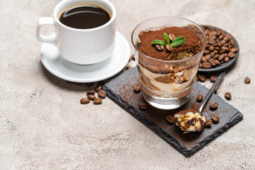 Portion of Classic tiramisu dessert in a glass cup on stone serving board and fres espresso coffee on concrete background
