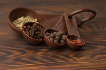 Set of spices - black pepper peas, clove, hot red pepper and exotic spice at the  measuring spoons. dark wood background 